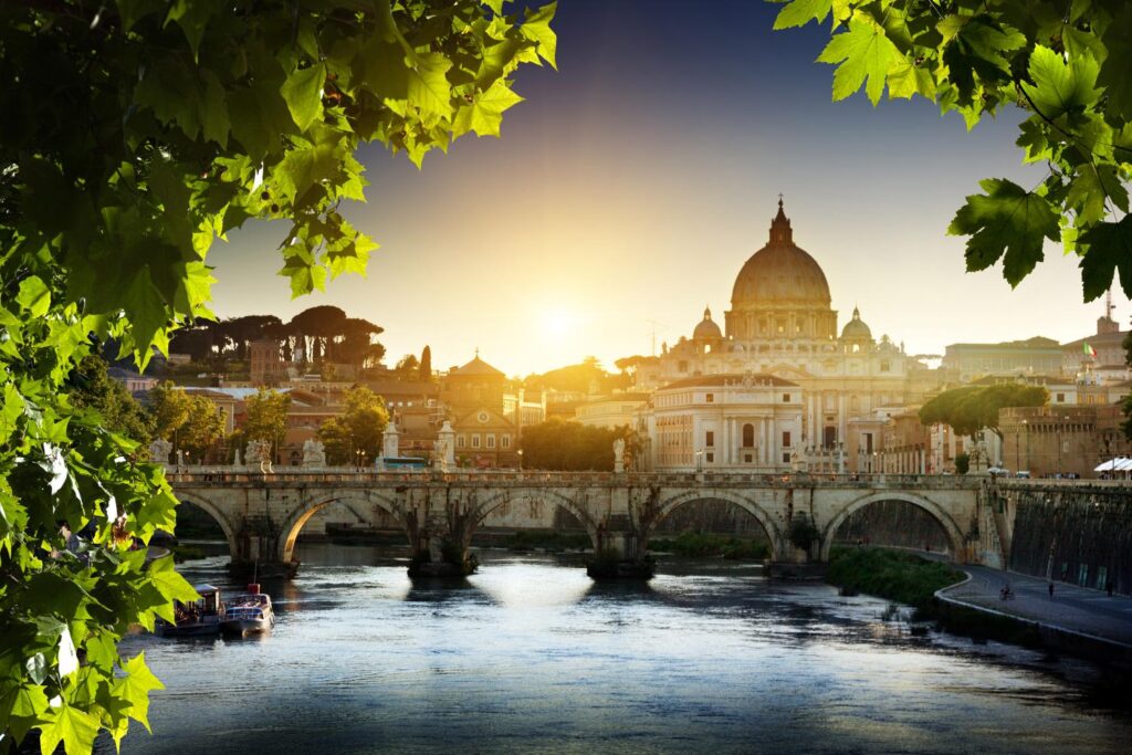 Sunrise view of St. Peter’s Basilica framed by green trees in Rome.