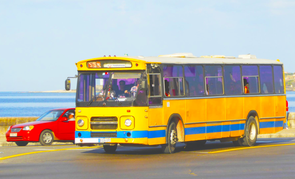 A yellow local bus driving along the Malecón in Havana, Cuba.